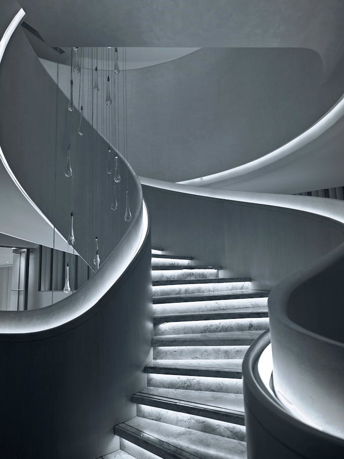 A modern, elegant spiral staircase with artistic lighting in a minimalist setting.